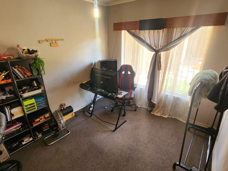 A bedroom space featuring carpeted flooring and a window with a curtain rod, currently utilized as a home office area.