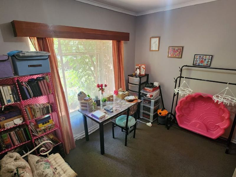 A bedroom featuring carpeted flooring and a large window with a timber pelmet, offering natural light and a view of the garden.