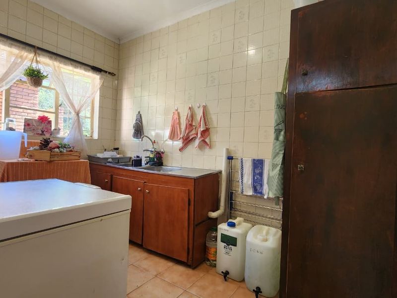 A functional laundry area featuring tiled walls, built-in wooden cabinetry, and a stainless steel sink, offering practical utility space with potential for modernization.