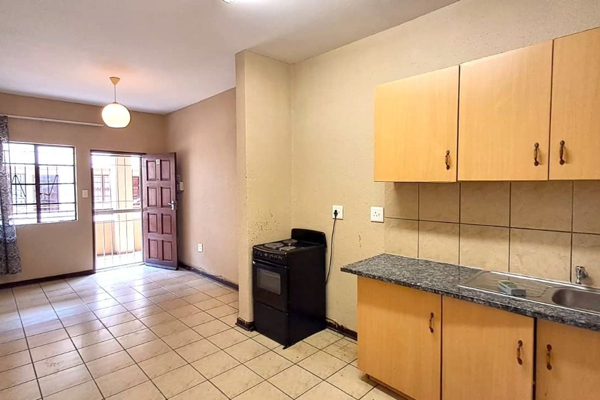 Open-plan living area featuring a functional kitchen with built-in cabinetry, tiled flooring, and direct access to an exterior security gate.
