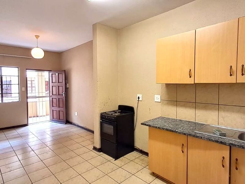 Open-plan living area featuring a functional kitchen with built-in cabinetry, tiled flooring, and direct access to an exterior security gate.