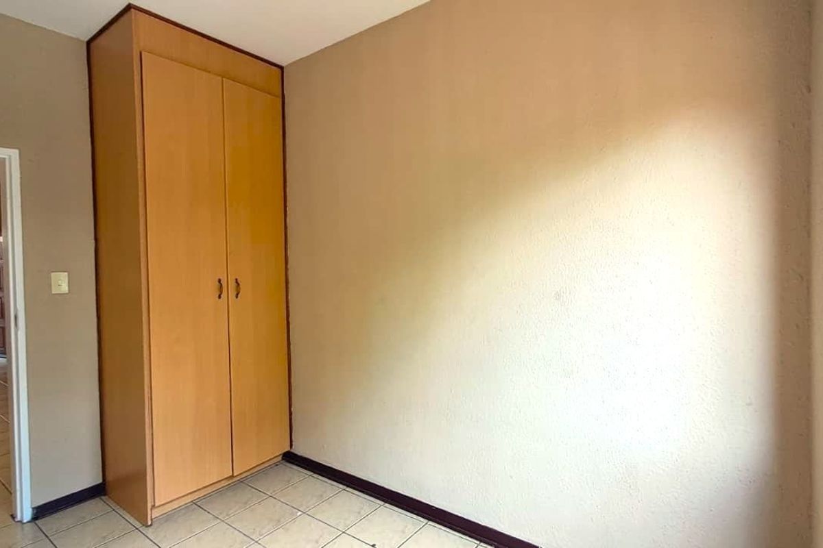 A clean, empty bedroom featuring neutral walls, tiled flooring, and a built-in wooden wardrobe, offering a blank canvas for personalization.