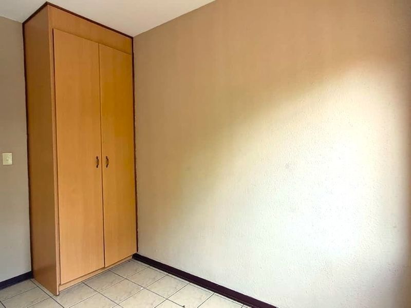 A clean, empty bedroom featuring neutral walls, tiled flooring, and a built-in wooden wardrobe, offering a blank canvas for personalization.