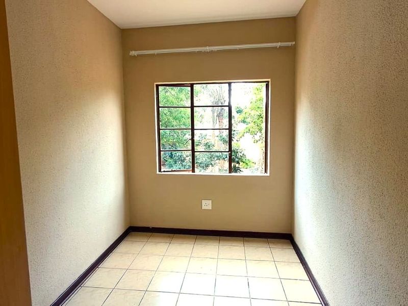 A vacant bedroom featuring neutral textured walls, tiled flooring, and a window with security bars, offering a clean and simple space.