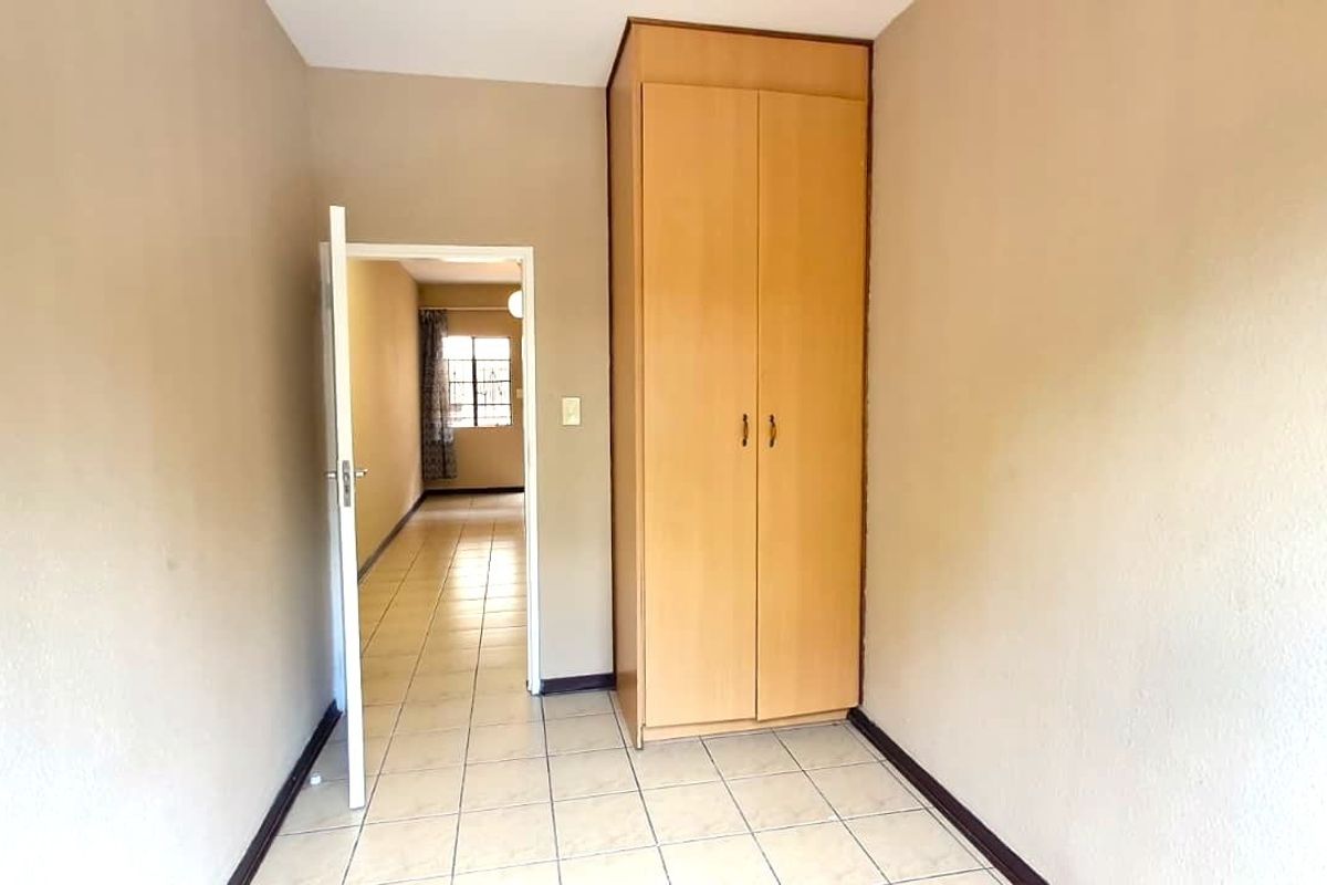 A clean, empty bedroom featuring neutral wall tones, tiled flooring, and a built-in wooden wardrobe, offering a versatile space for customization.