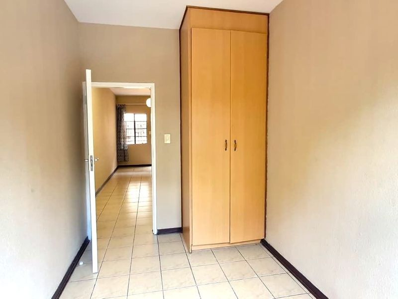 A clean, empty bedroom featuring neutral wall tones, tiled flooring, and a built-in wooden wardrobe, offering a versatile space for customization.
