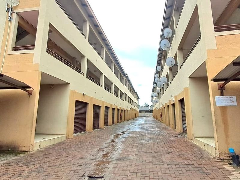 Exterior view of an apartment complex featuring a paved driveway, multiple garage units, and upper-level balconies with satellite dish installations.