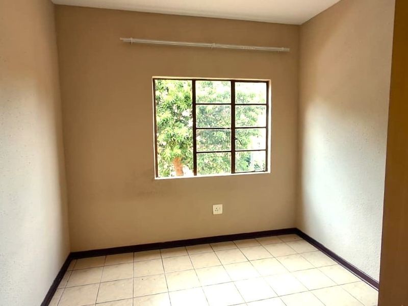 A vacant bedroom featuring neutral wall tones, tiled flooring, and a steel-framed window with an integrated curtain rail.