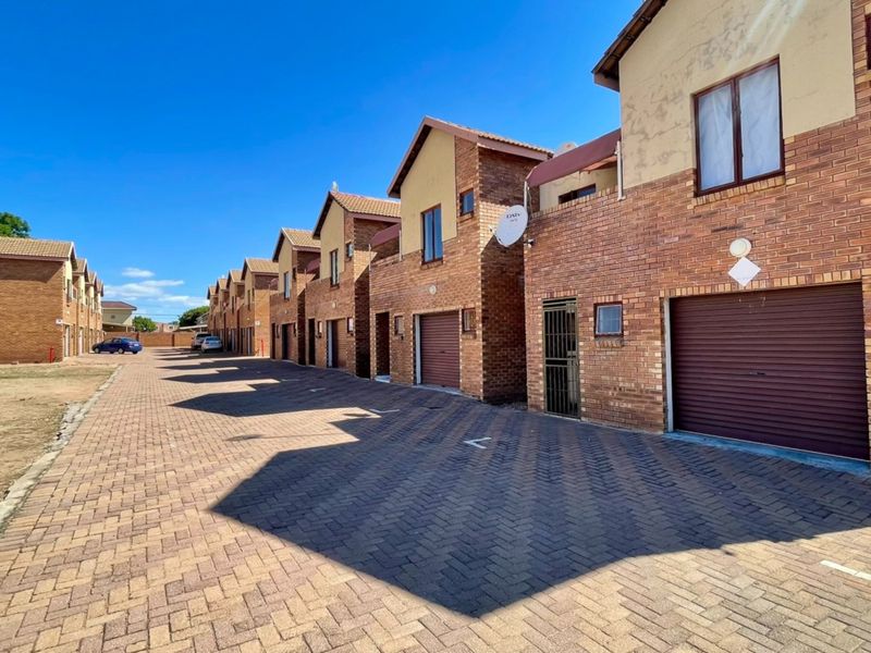 A view of a townhouse complex featuring face brick facades, paved driveways, and individual roll-up garage doors.
