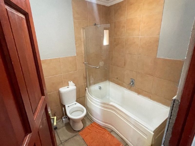 A functional bathroom featuring a bathtub with a glass shower screen, toilet, and neutral wall tiling, ready for modern updates.