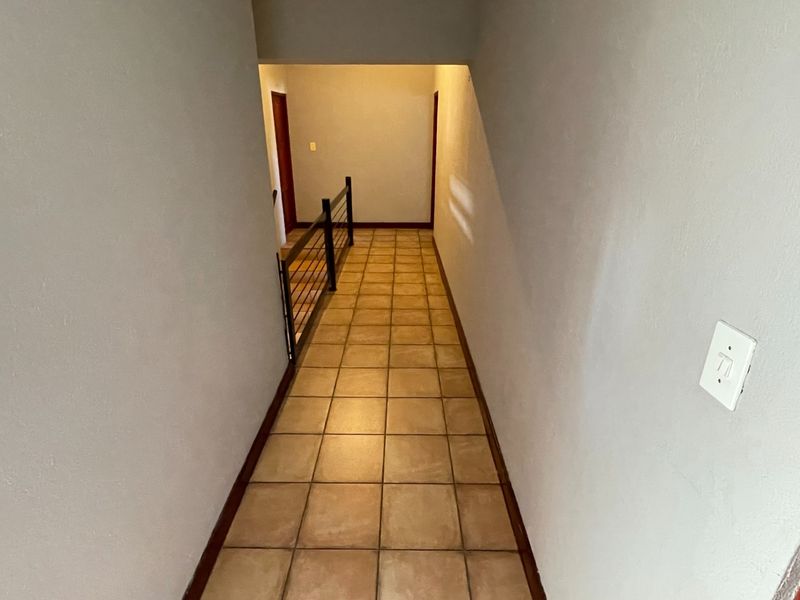 A clean, empty hallway featuring tiled flooring and a metal balustrade, leading towards an interior doorway.