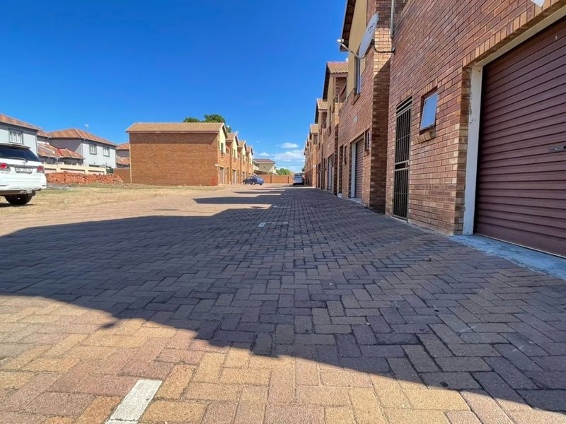 A view of the townhouse complex driveway featuring brick paving, face brick facades, and multiple garage access points.