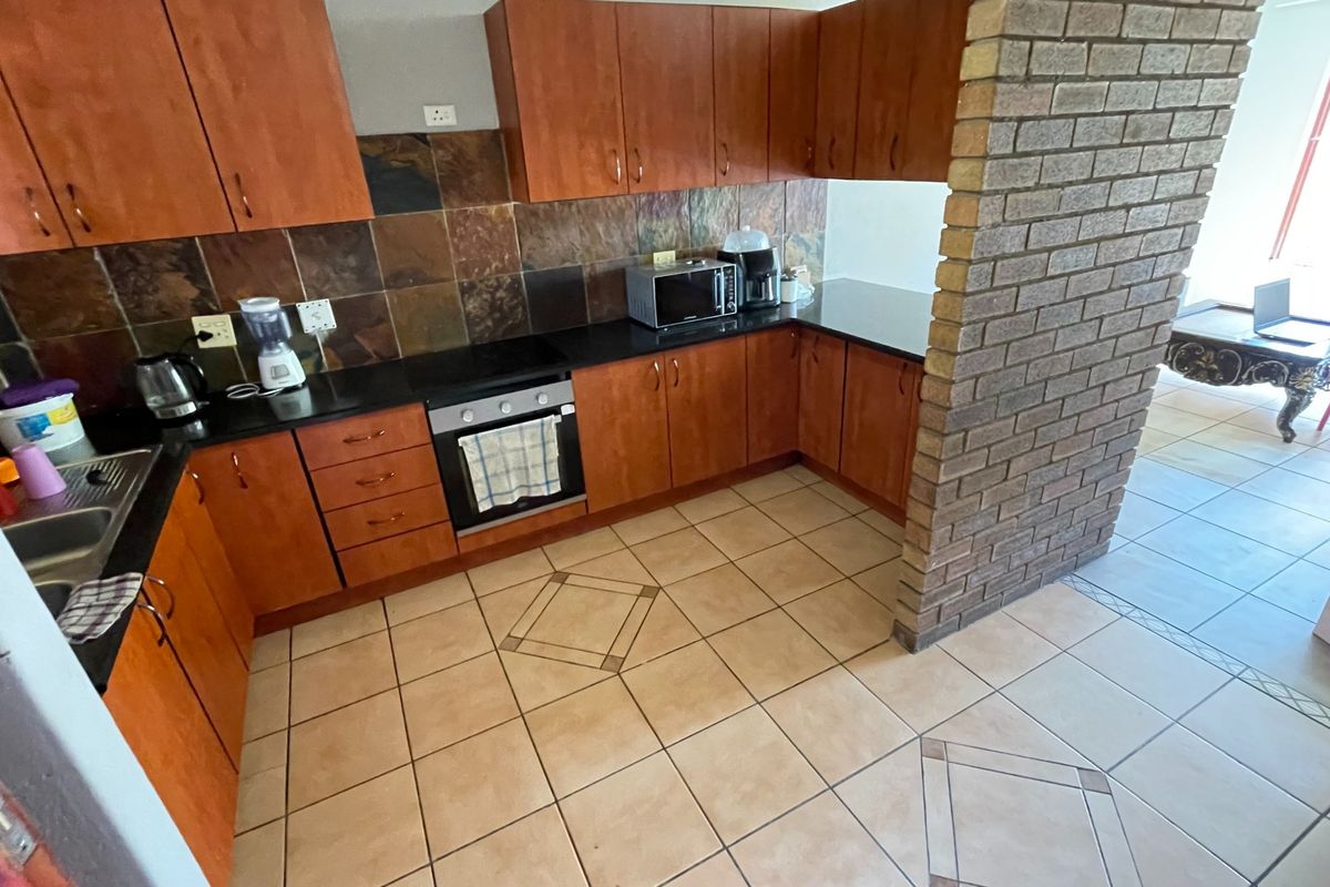 A functional kitchen featuring wood-finish cabinetry, dark stone countertops, a built-in oven, and a distinctive exposed brick pillar separating the space from the living area.