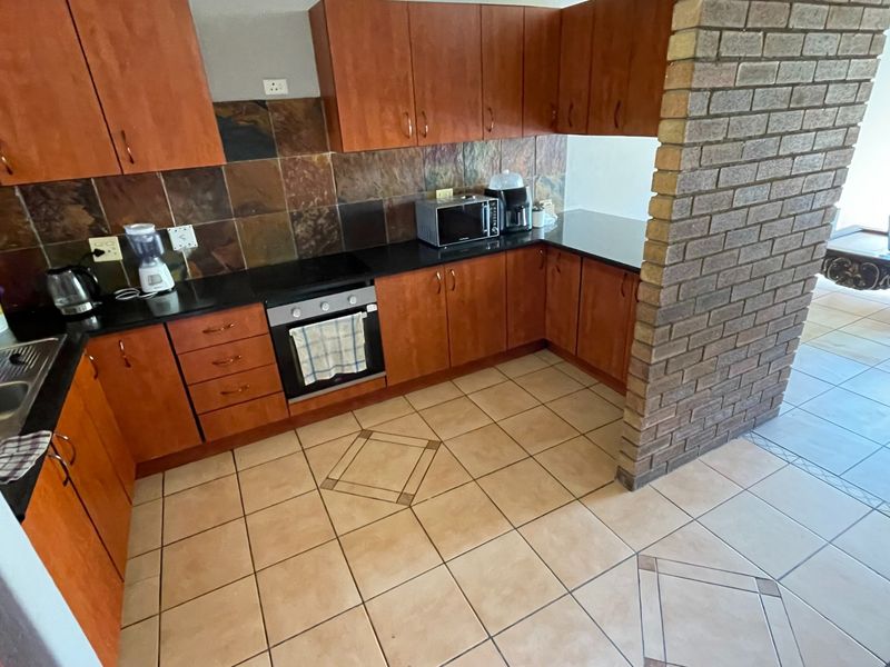 A functional kitchen featuring wood-finish cabinetry, dark stone countertops, a built-in oven, and a distinctive exposed brick pillar separating the space from the living area.