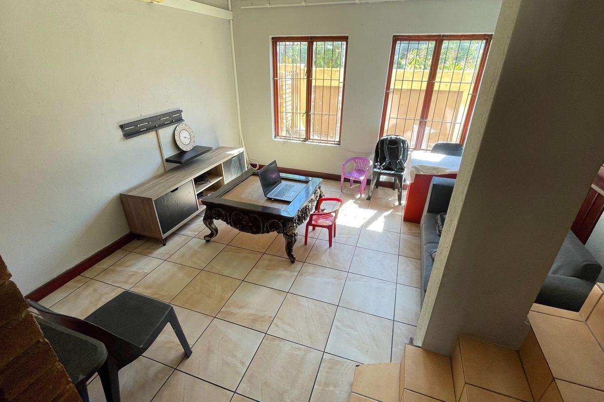 A living room area featuring tiled flooring, timber-framed windows with security bars, and a wall-mounted television bracket.