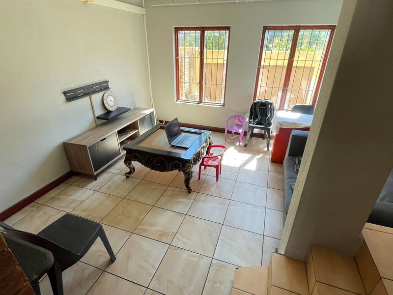 A living room area featuring tiled flooring, timber-framed windows with security bars, and a wall-mounted television bracket.