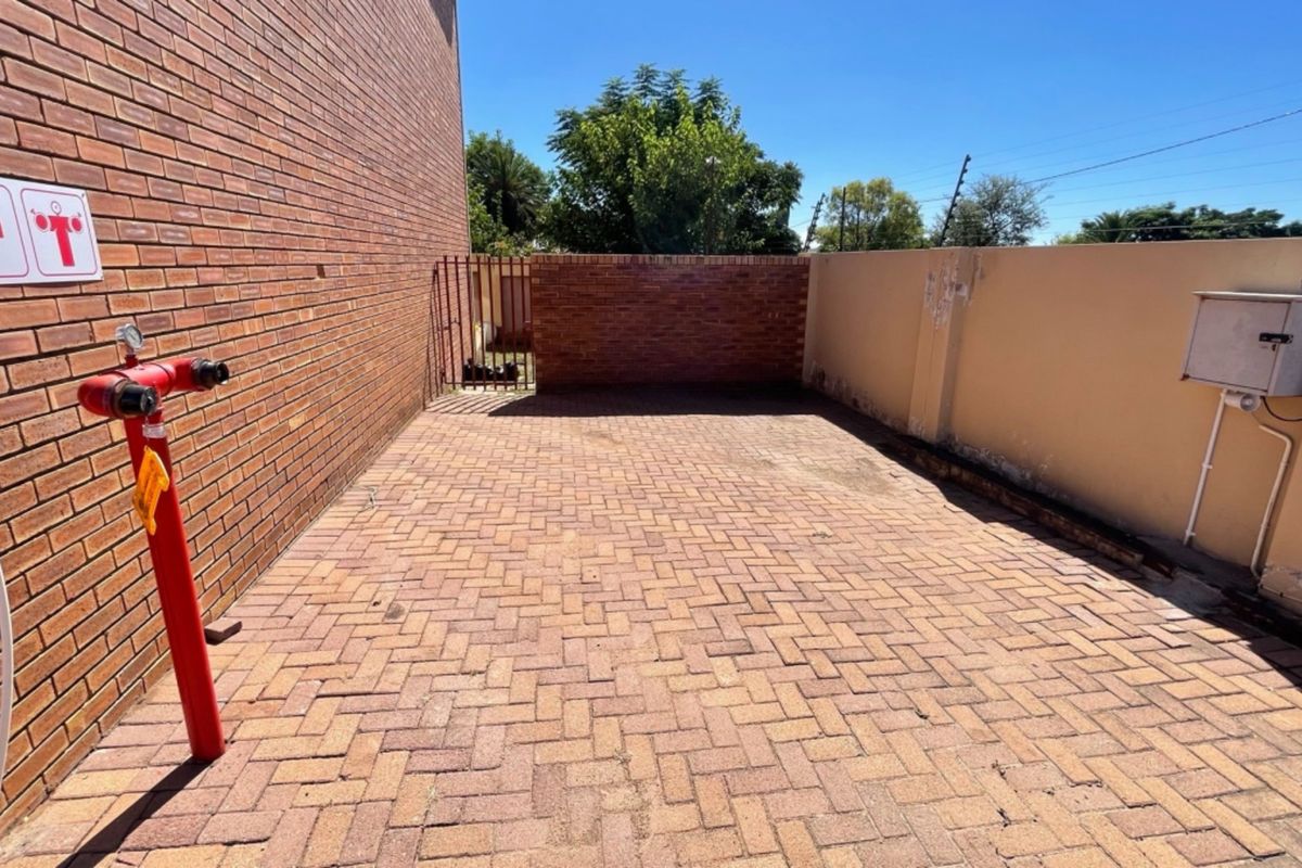 A paved rear courtyard area featuring a fire hydrant, enclosed by brick and plastered perimeter walls with electric fencing.