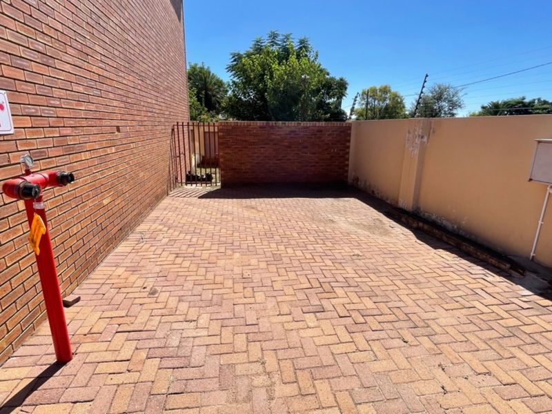 A paved rear courtyard area featuring a fire hydrant, enclosed by brick and plastered perimeter walls with electric fencing.