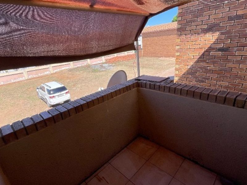 A compact outdoor balcony featuring a brick wall, tiled flooring, and a retractable shade awning, overlooking the property grounds.