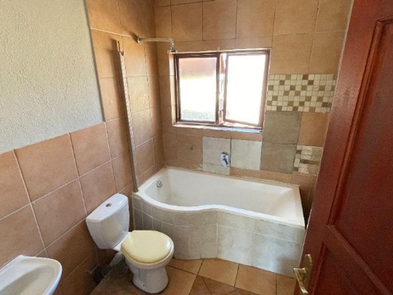 A functional bathroom featuring a corner bathtub with shower attachment, a standard toilet, and a washbasin, finished with dated ceramic wall and floor tiles.