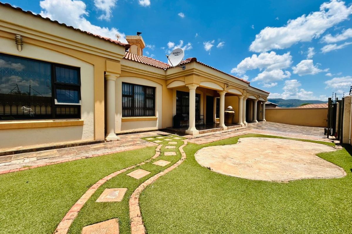 Rear view of the house featuring a covered patio with columns, artificial lawn, and a stone paver pathway leading to the entrance.
