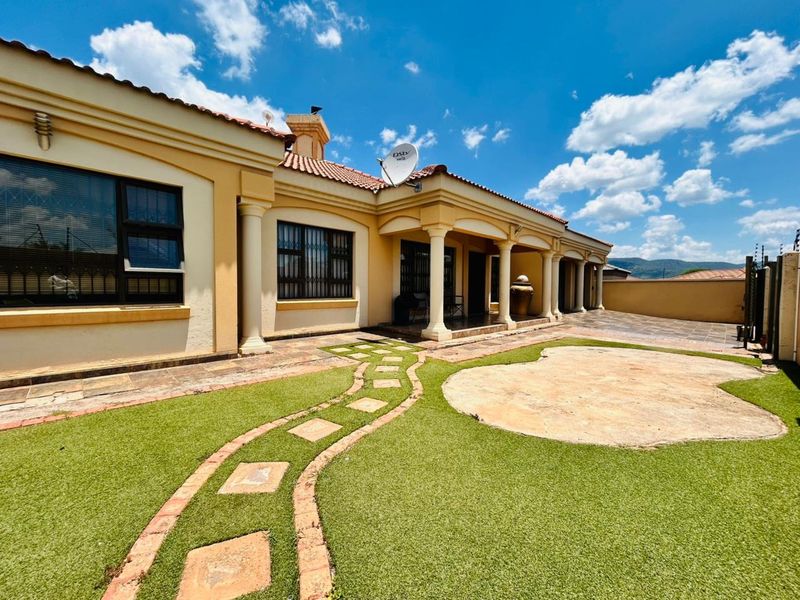 Rear view of the house featuring a covered patio with columns, artificial lawn, and a stone paver pathway leading to the entrance.