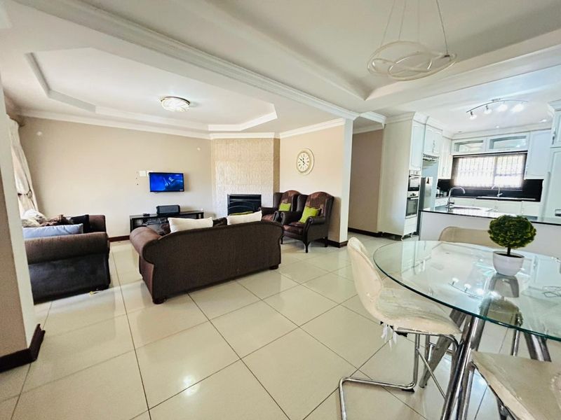 Spacious open-plan living area featuring a tray ceiling, built-in fireplace, and a modern kitchen with integrated cabinetry and tiled flooring throughout.