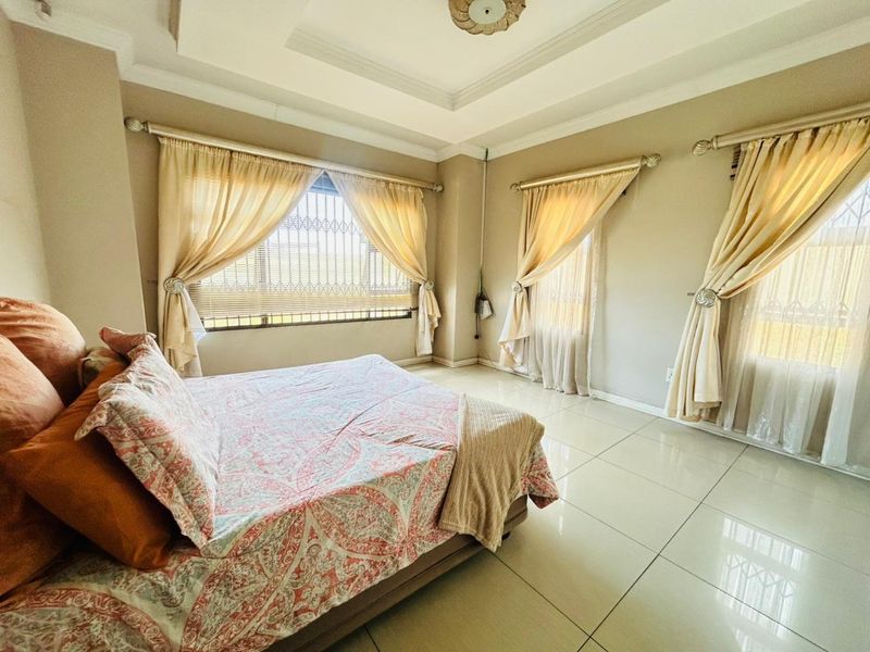 Spacious bedroom featuring neutral walls, large windows with security bars, elegant tray ceiling, and polished tile flooring.