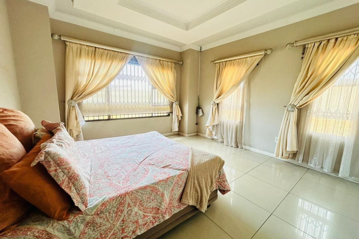 Spacious bedroom featuring neutral walls, large windows with security bars, elegant tray ceiling, and polished tile flooring.