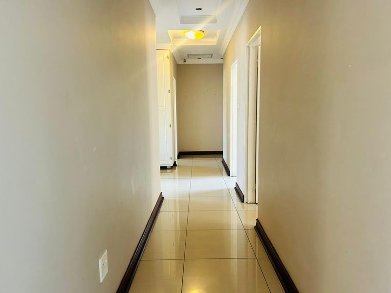 A clean, well-lit hallway featuring neutral tiled flooring, recessed ceiling lighting, and built-in storage cabinetry, providing a bright and functional transition space.