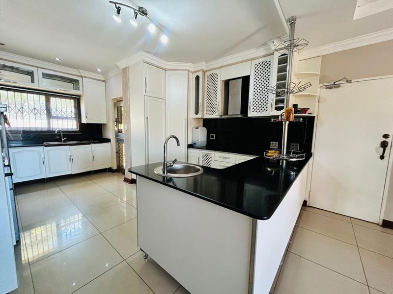 A well-maintained kitchen featuring white cabinetry, black granite countertops, a central island with a sink, and tiled flooring.
