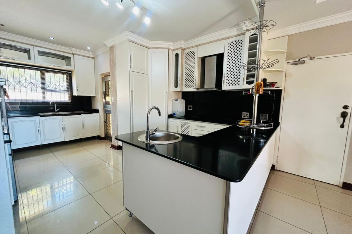 A well-maintained kitchen featuring white cabinetry, black granite countertops, a central island with a sink, and tiled flooring.