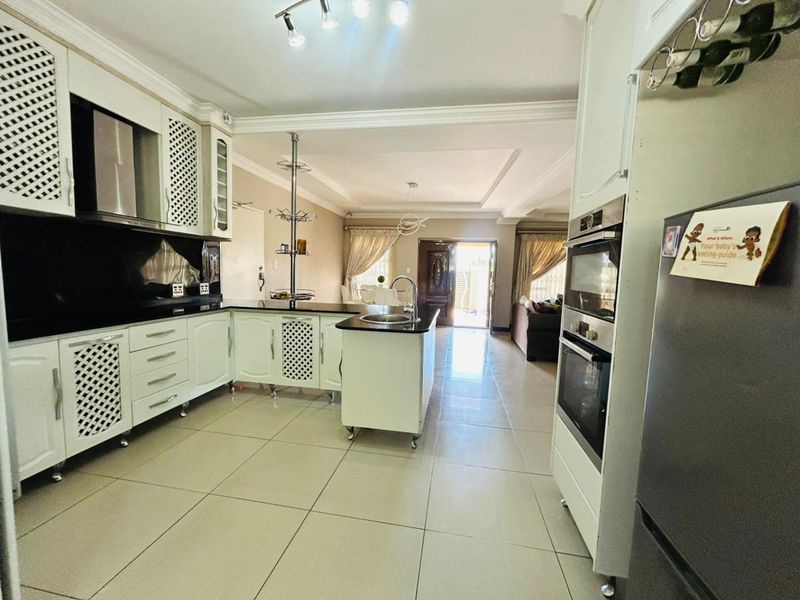 Spacious open-plan kitchen featuring white cabinetry, a central island, integrated double wall oven, and sleek tiled flooring, flowing into the adjacent living area.
