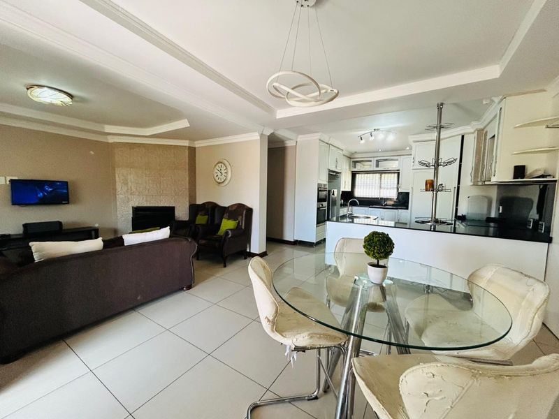 Spacious open-plan living and dining area featuring a stone-clad fireplace, tiled flooring, and a modern kitchen with granite countertops and built-in appliances.