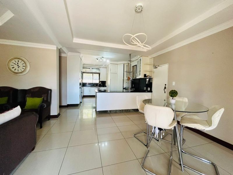 An open-plan living and kitchen area featuring tiled flooring, a central kitchen island, and modern cabinetry with a clean, neutral aesthetic.