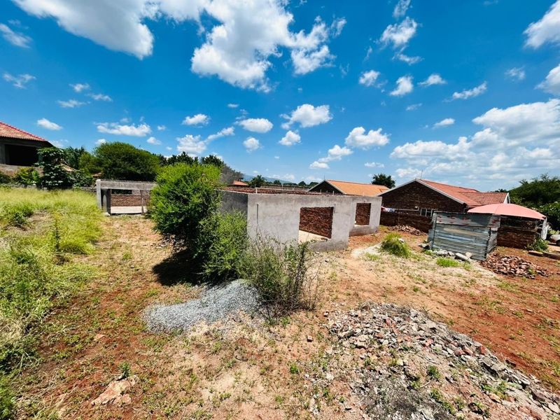A view of a residential plot featuring an unfinished masonry structure and unimproved land, offering potential for further development.