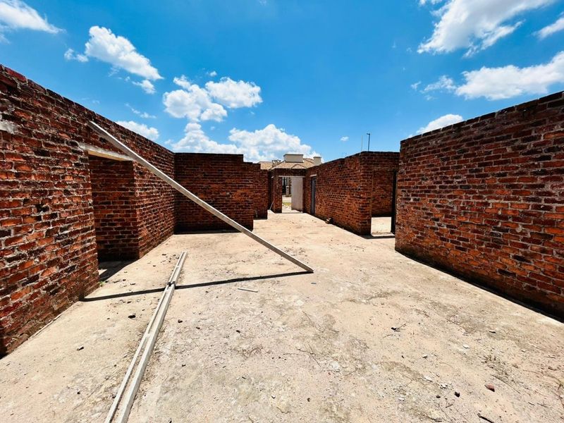 An unfinished residential structure featuring exposed brick walls and a concrete slab foundation, currently in the early stages of construction.
