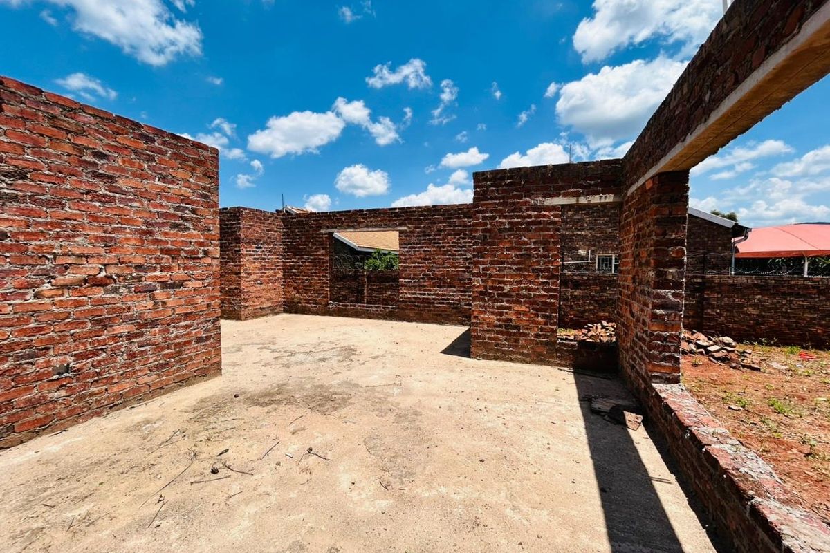 An unfinished residential construction site showing exposed brick walls and a concrete slab foundation under a clear blue sky.