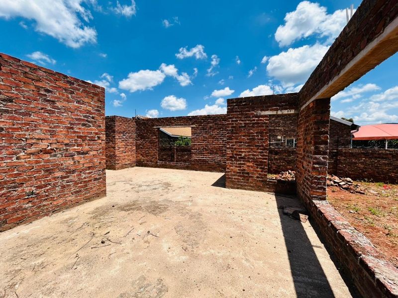 An unfinished residential construction site showing exposed brick walls and a concrete slab foundation under a clear blue sky.