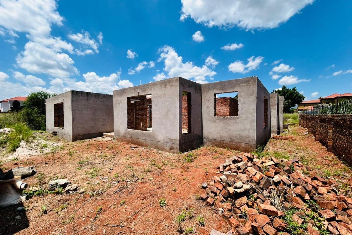 An unfinished residential structure in the early stages of construction, featuring exposed concrete block walls on a vacant plot of land.