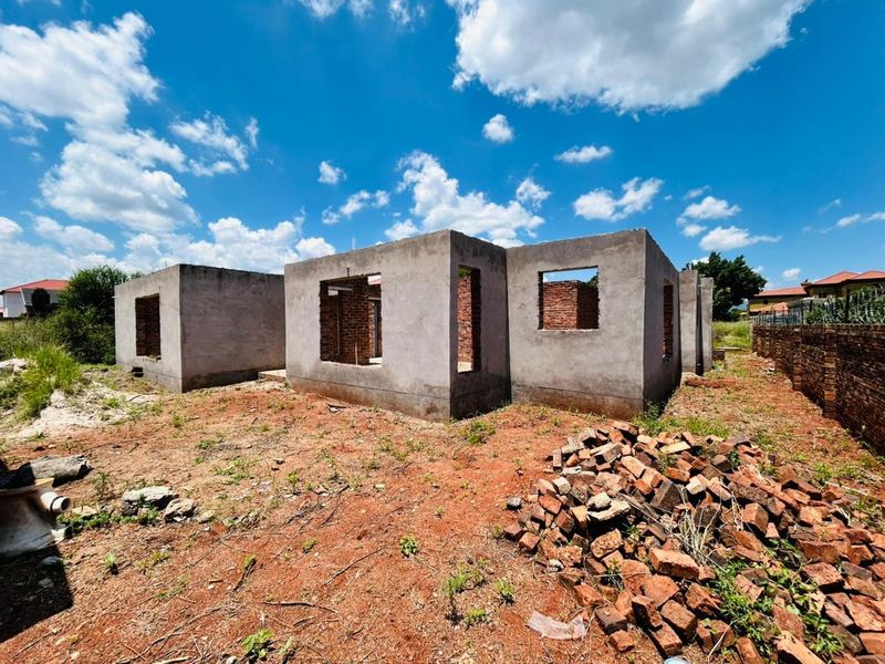 An unfinished residential structure in the early stages of construction, featuring exposed concrete block walls on a vacant plot of land.