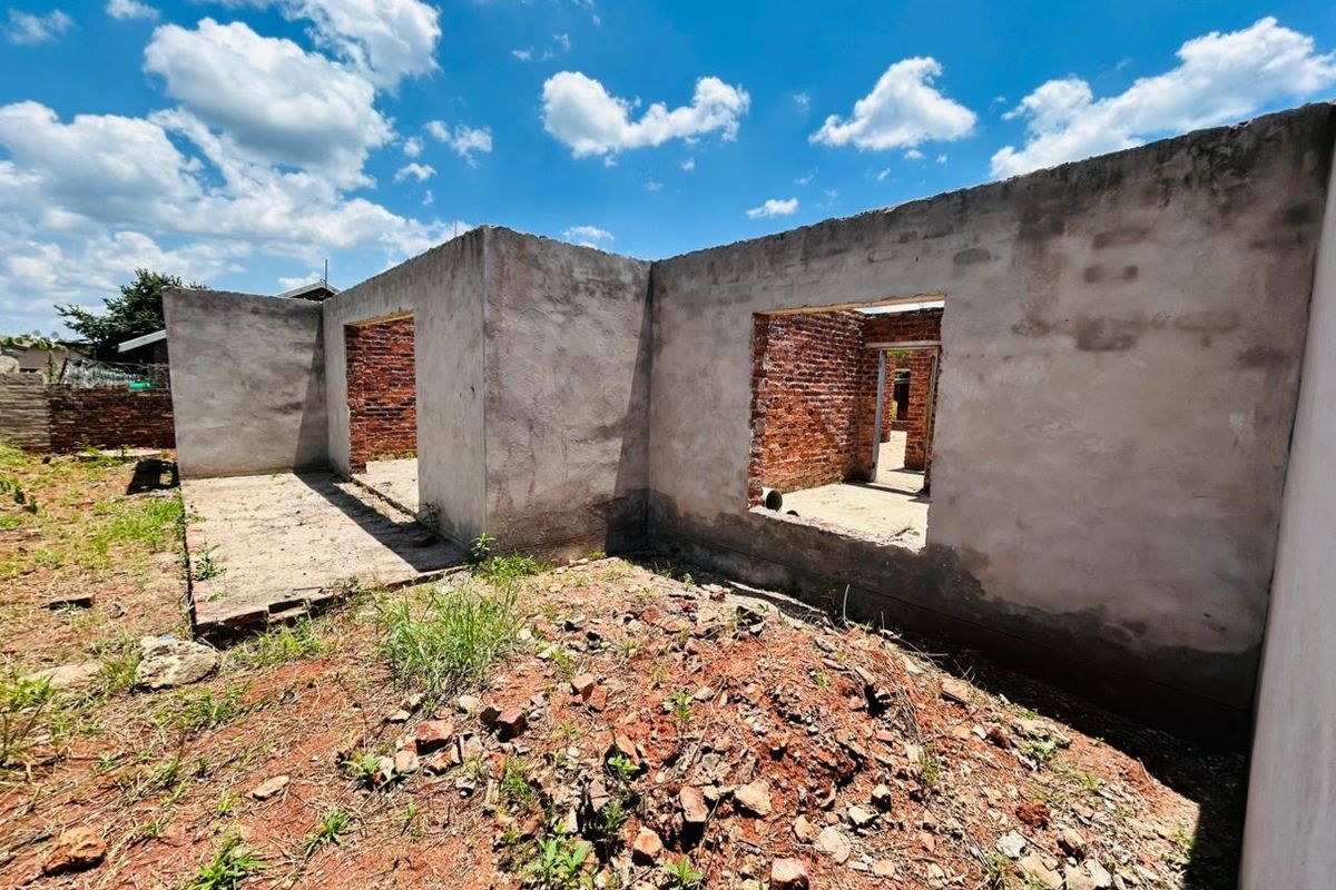 An exterior view of a residential property under construction, featuring exposed brickwork and unfinished cement rendered walls on a concrete slab foundation.