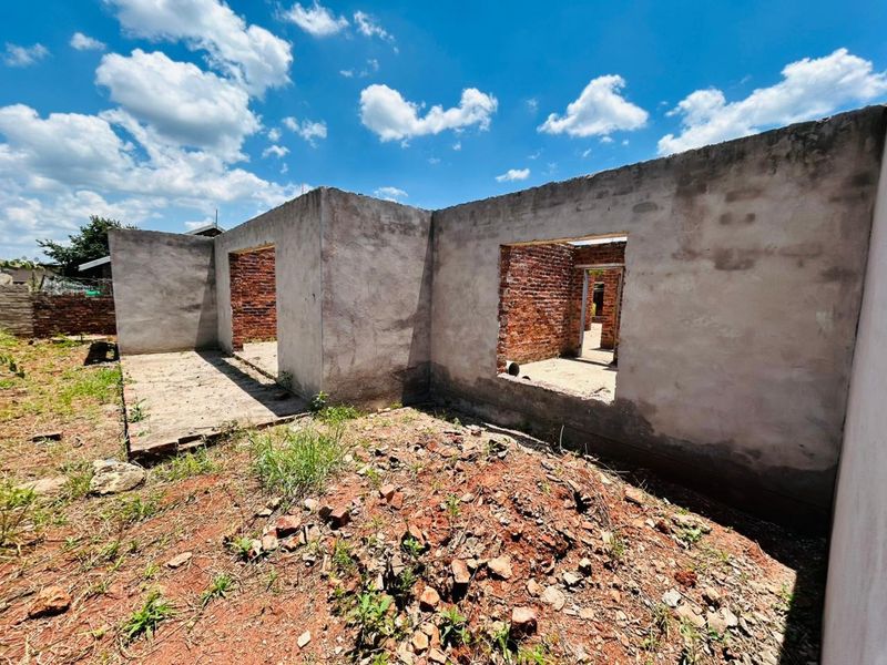 An exterior view of a residential property under construction, featuring exposed brickwork and unfinished cement rendered walls on a concrete slab foundation.