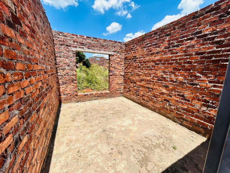 An unfinished room structure featuring exposed brick walls and a concrete floor, currently in the early stages of construction.
