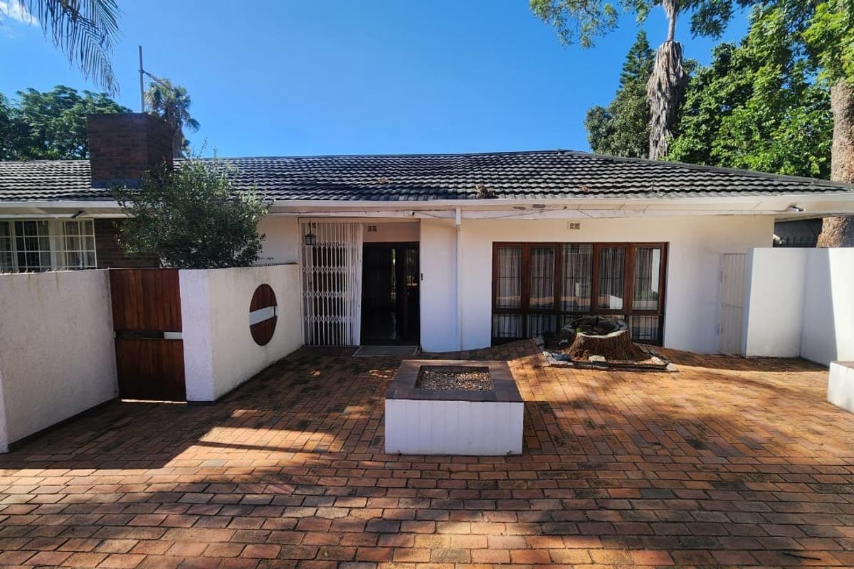 Rear exterior view featuring a brick-paved patio area with a built-in fire pit, tiled roof, and secure access to the main dwelling.