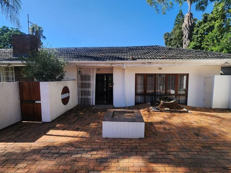 Rear exterior view featuring a brick-paved patio area with a built-in fire pit, tiled roof, and secure access to the main dwelling.
