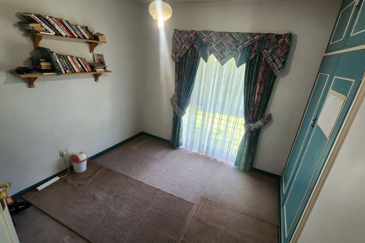 A compact bedroom featuring built-in wardrobe storage, carpeted flooring, and a window with curtains.