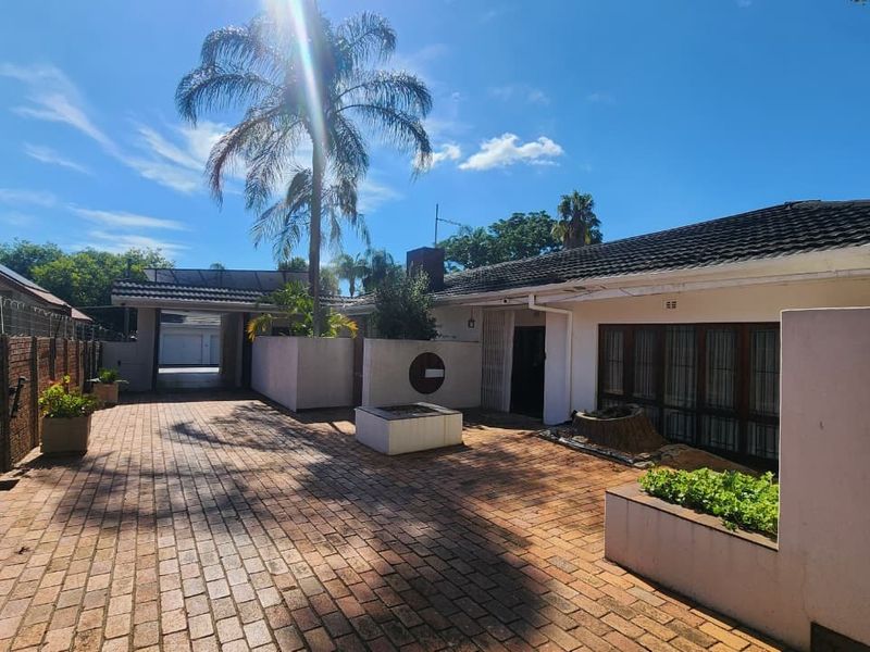 Front exterior view featuring a brick paved driveway, covered carport, and established garden beds with boundary walling.