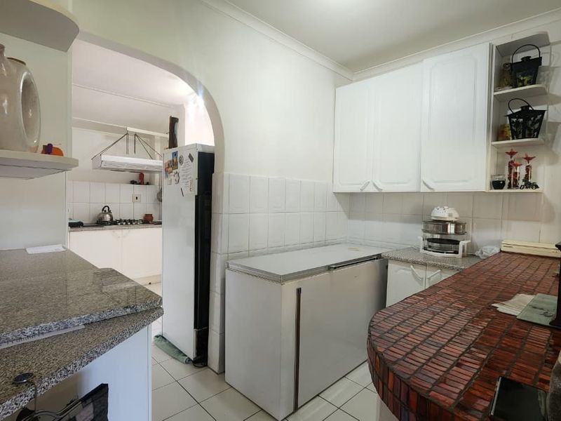 Functional scullery area featuring built-in cabinetry, tiled splashbacks, and a breakfast bar, providing additional prep space adjacent to the main kitchen.