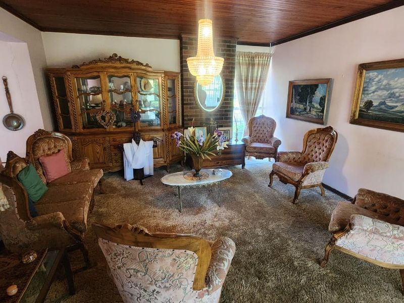 A traditional living room featuring a brick fireplace, timber ceiling, and carpeted flooring, offering a classic layout with potential for modern updates.